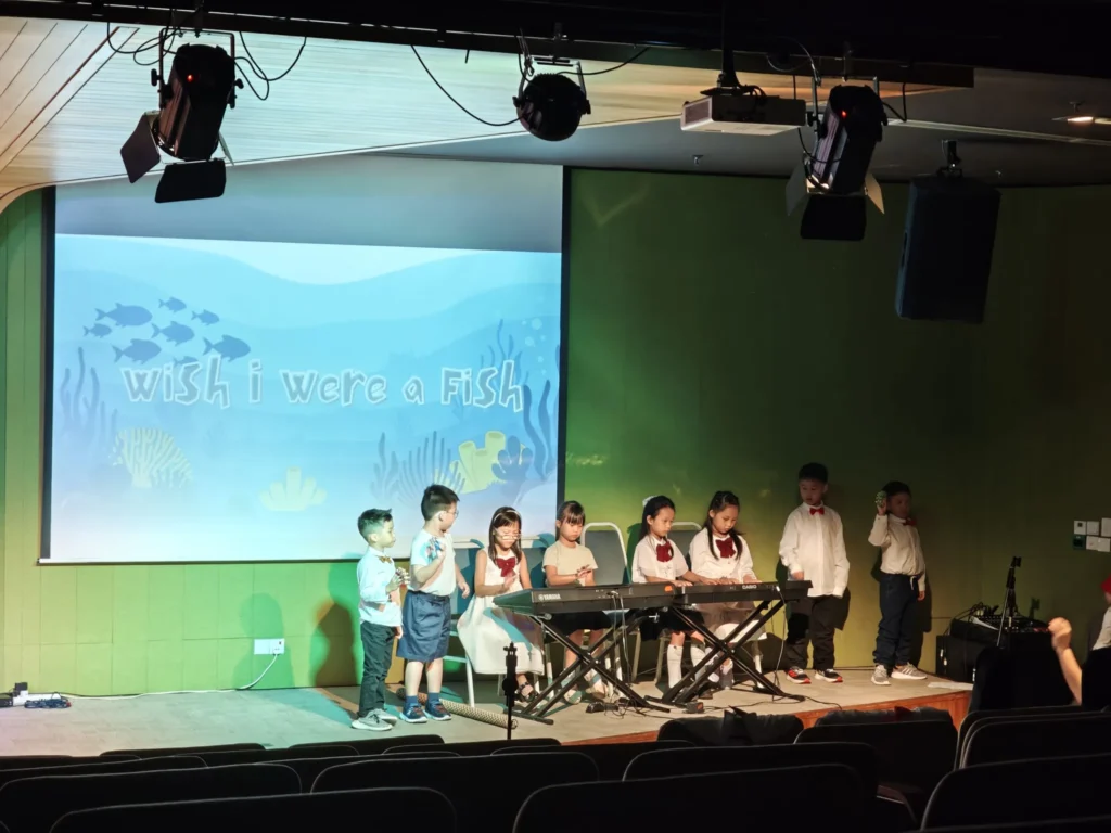 Children singing beside keyboards on a Theatrette stage