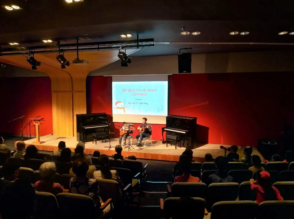 Musicians performing between two pianos on a Theatrette stage at a Christmas charity concert