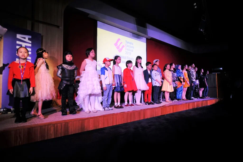 Children in costumes lined up on the Theatrette stage at the Yamaha Electone Festival