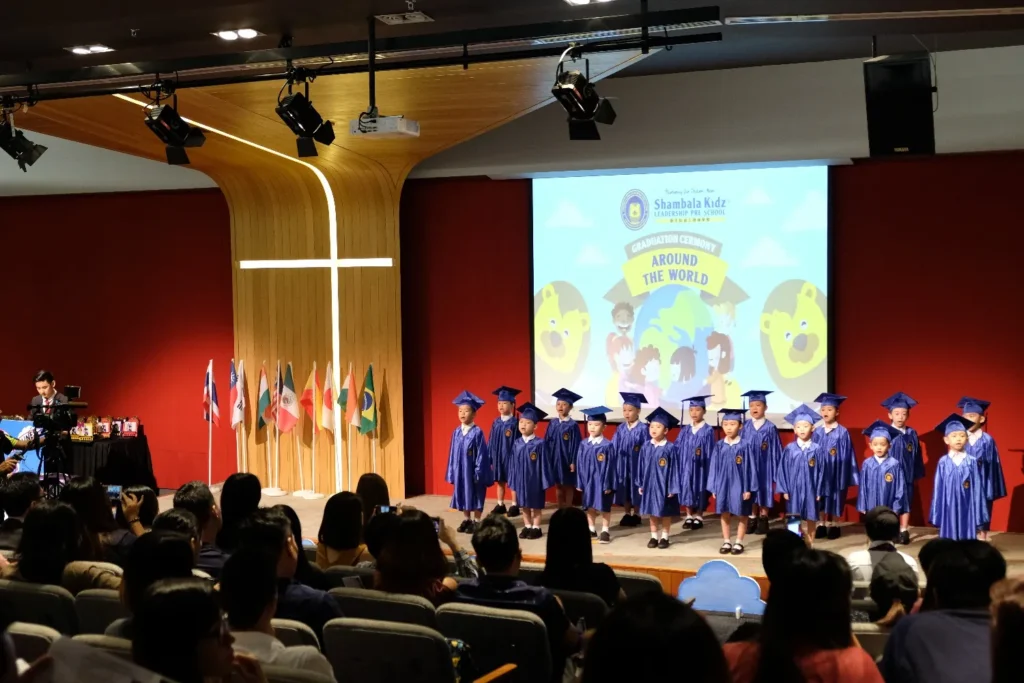 Kindergarten children in caps and gowns on stage before a full Theatrette audience