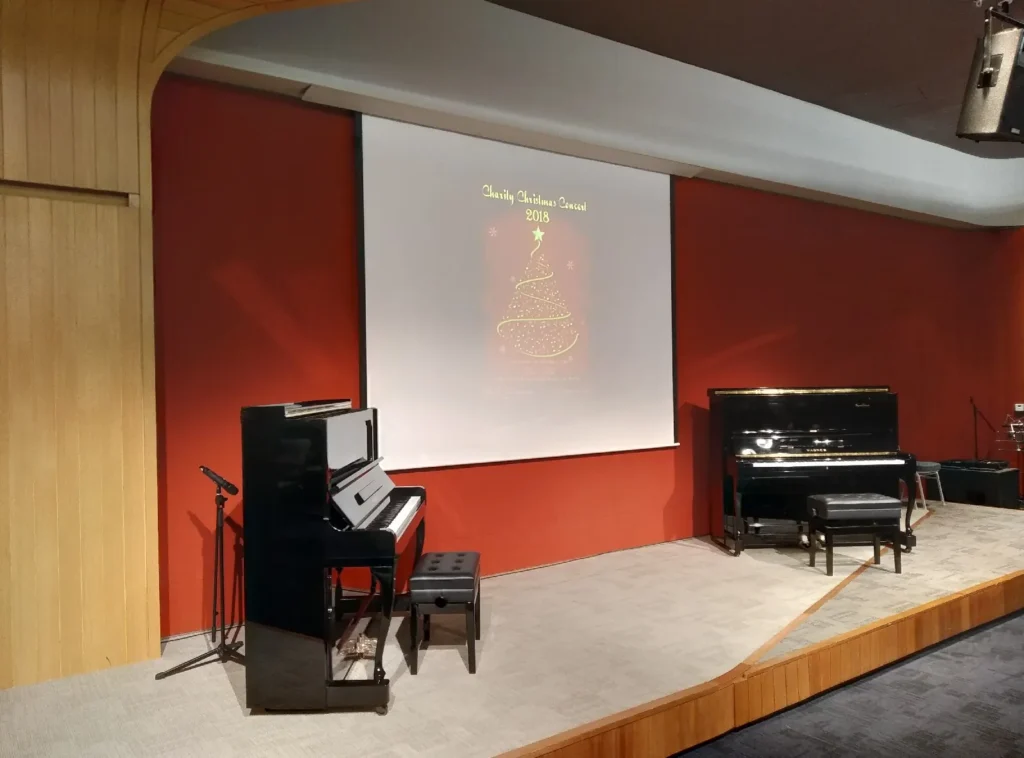 Upright pianos on a Theatrette stage under a Christmas concert screen