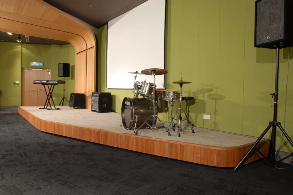 Theatrette stage with a drum kit, speakers and a screen against a green wall