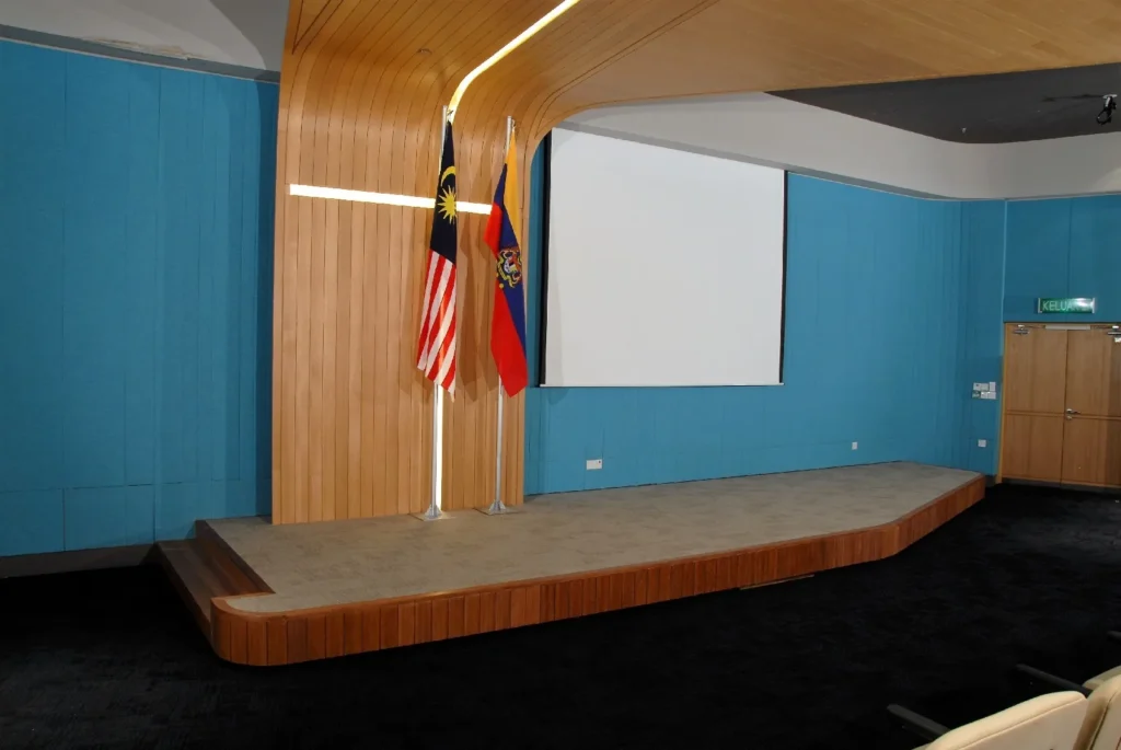 Theatrette stage with the Malaysian flag and the Federal Territories flag beside a projector screen