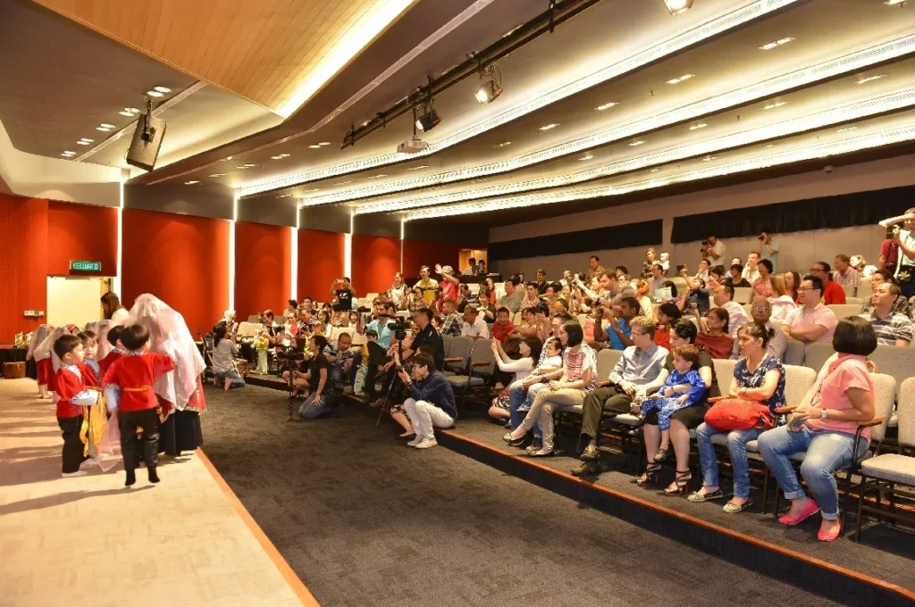 Families filling the tiered seats of a Theatrette at a kindergarten concert
