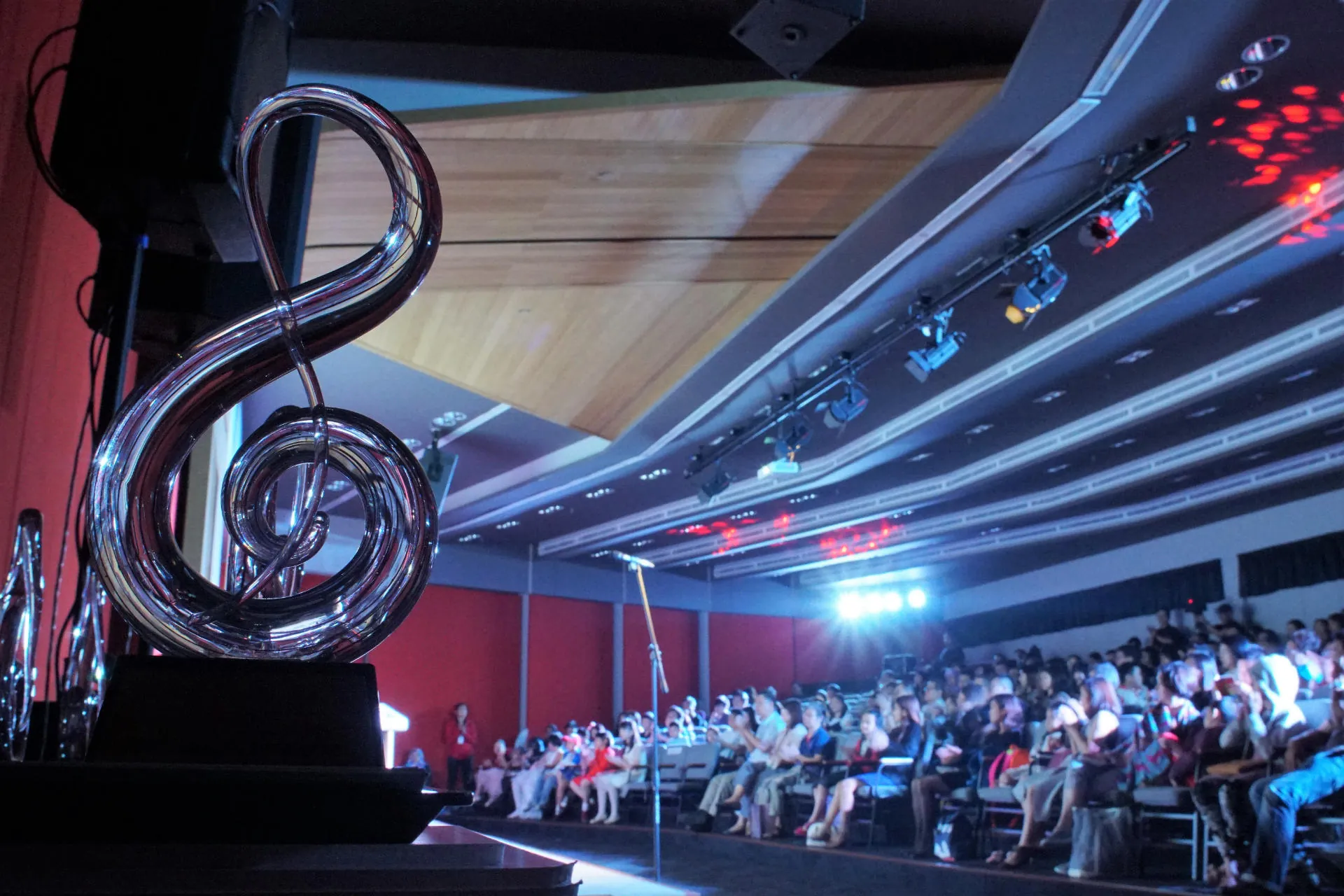 Treble clef sculpture beside the stage, with a full audience in a Theatrette